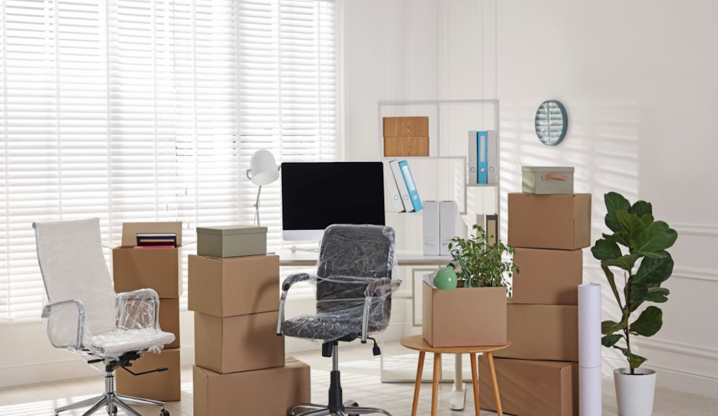 Office relocation boxes, desks and chairs packed in a bright modern workspace.