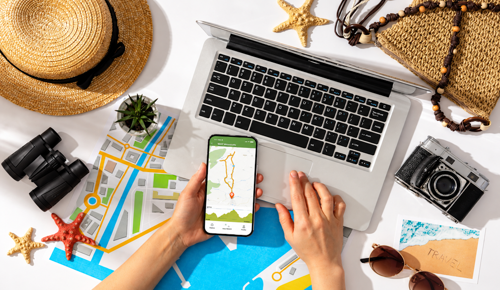 Traveller planning a trip on a laptop and phone map with a hat, camera and sunglasses, booking Bali day tours such as ATV and rafting and a yacht charter through a yacht broker