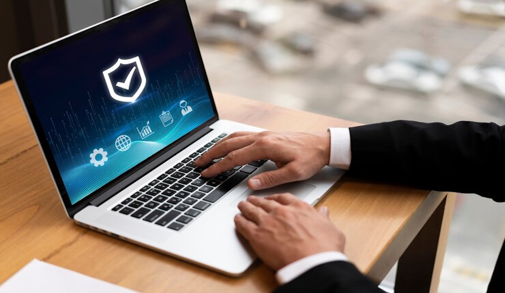 Person typing on a laptop with a security shield icon, representing cyber insurance basics.